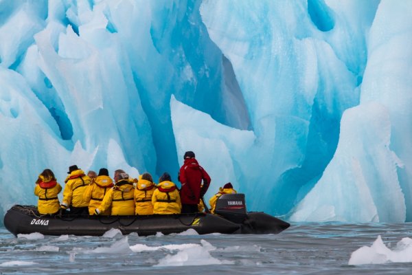 People in yellow jackets on a zodiac in front of a large wall of ice