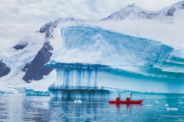 A red kayak in front of a large iceberg in Antarctica