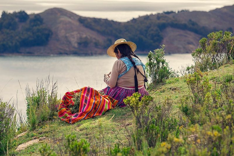 Peruvian woman on traditional clothes sitting in front of the lake.